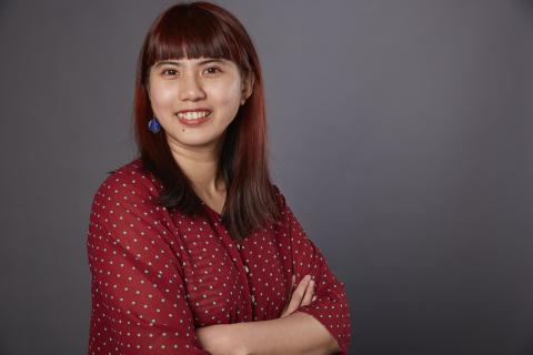 Smiling taiwanese woman with medium-long red hair facing the camera, body at an angle with arms crossed