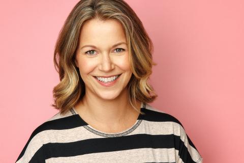 a woman with dark blonde hair facing the camera and smiling, pink background