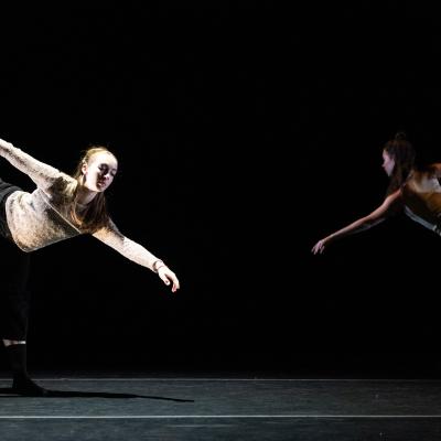 two dancers (one in foreground, one in background), in poses with one leg raised and arms out