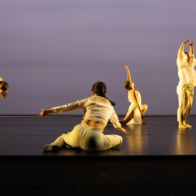 five dancers in various poses at various levels, light outfits with a darker background