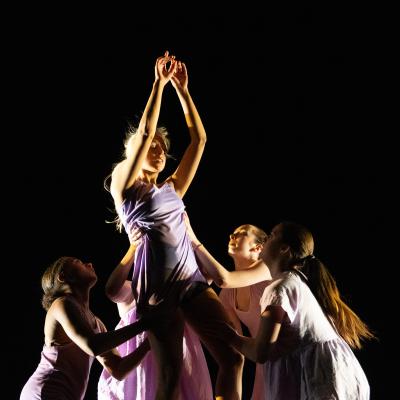 five dancers, four surrounding the fifth and holder her up, fifth dancer's arms raised and hands together
