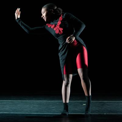 single dancer in pose, dark hair, dark outer garment, red top and shorts