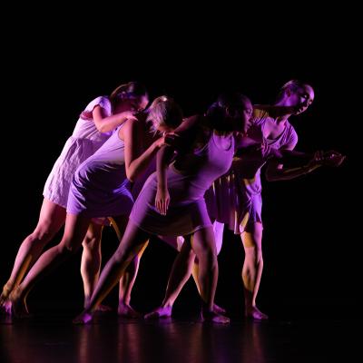 five dancers all linked by touch, in motion leaning to their left with bent posture