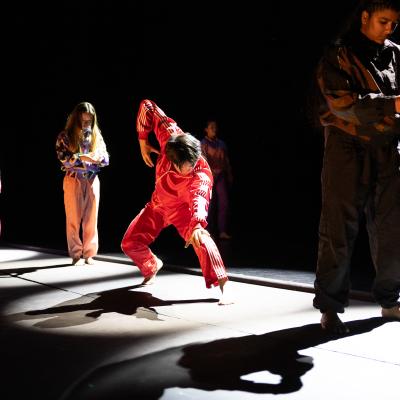 four dancers, each in a spotlight, in colorful outfits, in various poses