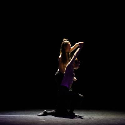 two dancers in poses on two different levels, each with an arm raised. 