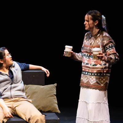 CAFE OF BABEL: An actor seated facing another actor, standing, holding two small starbucks cups.