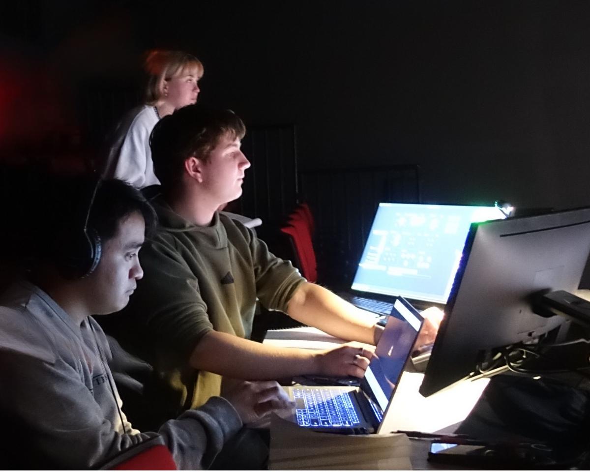 Three student designers watch a run-through from the design table.