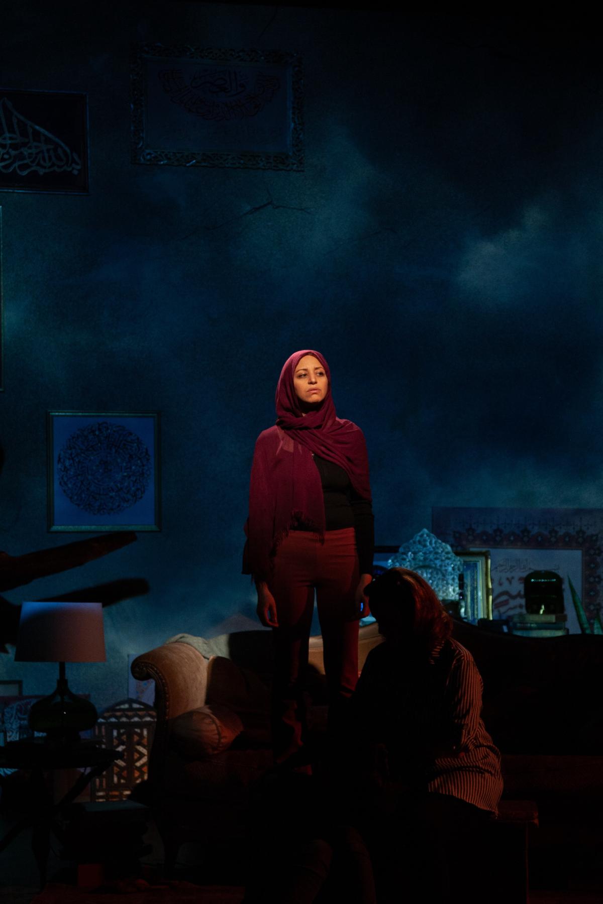 Woman in a hijab under stage lighting, looking out and up into the distance.