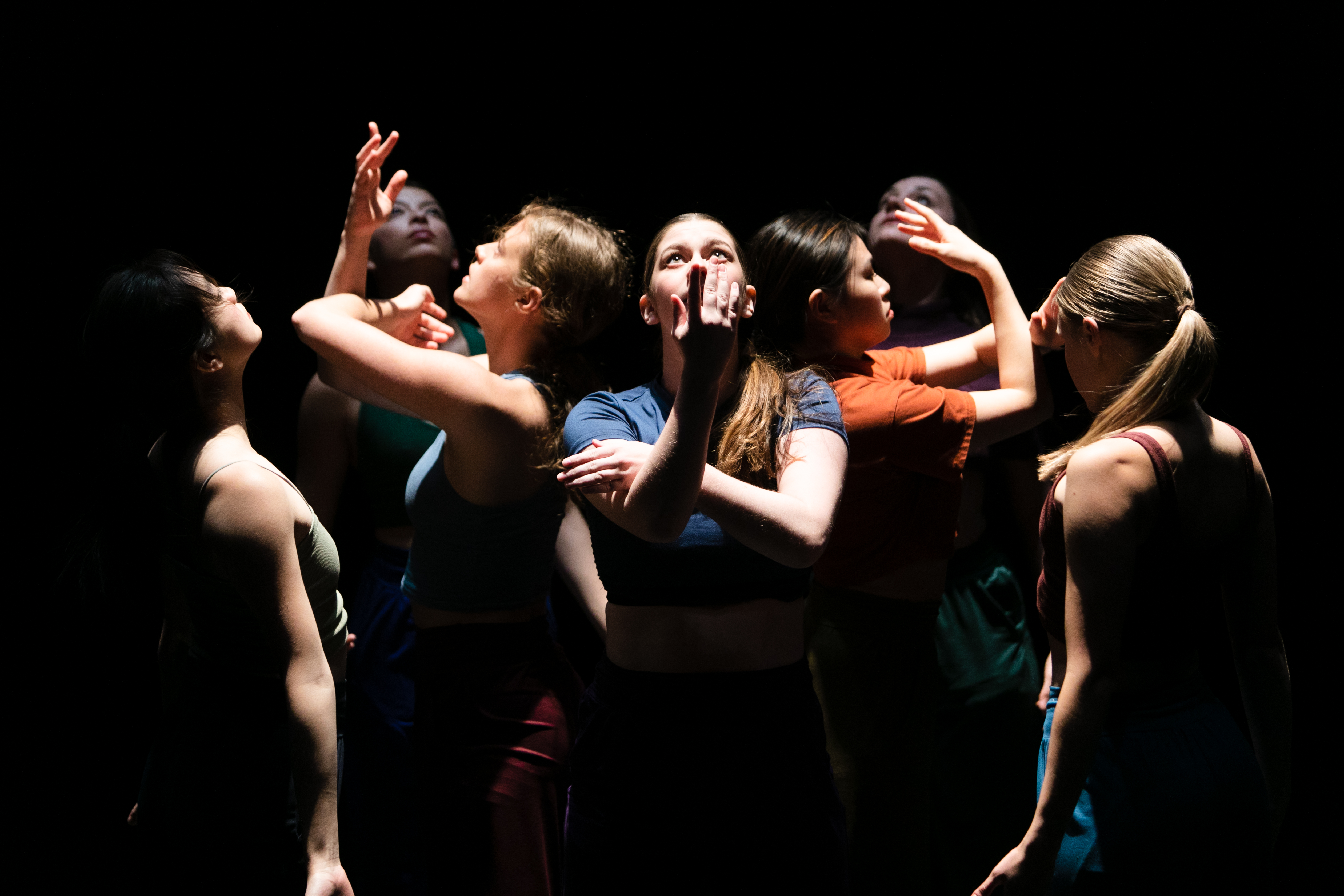 8 dancers in a spotlight in various poses, most looking up toward the light.