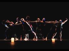 Dancers on stage in multiple poses, dark background, candles on the floor.