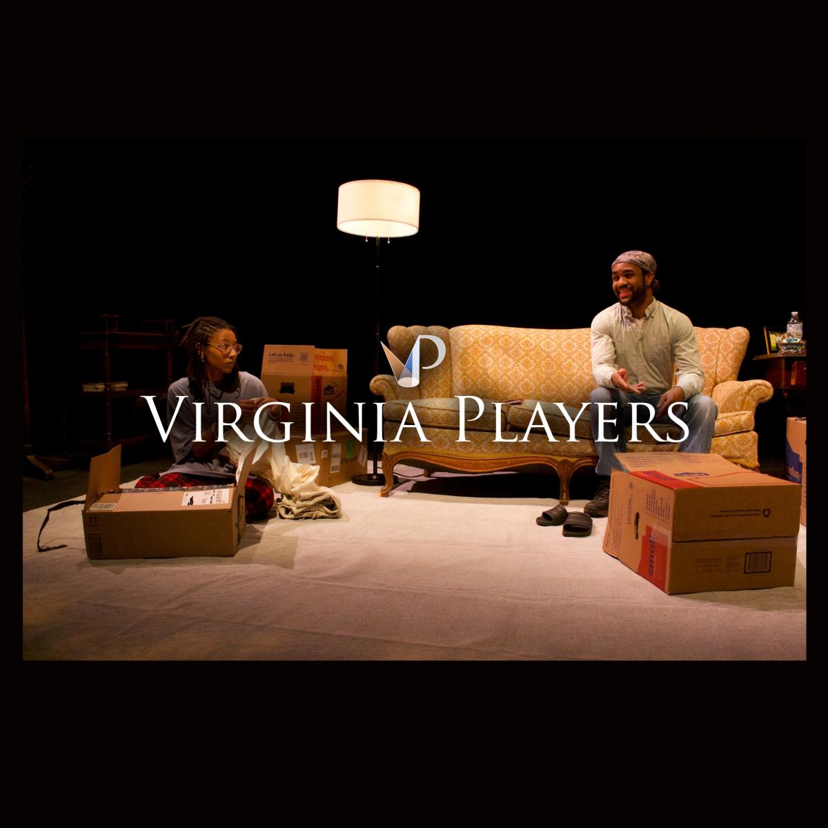 Two actors on a set of a living room with couch, lamp, and boxes